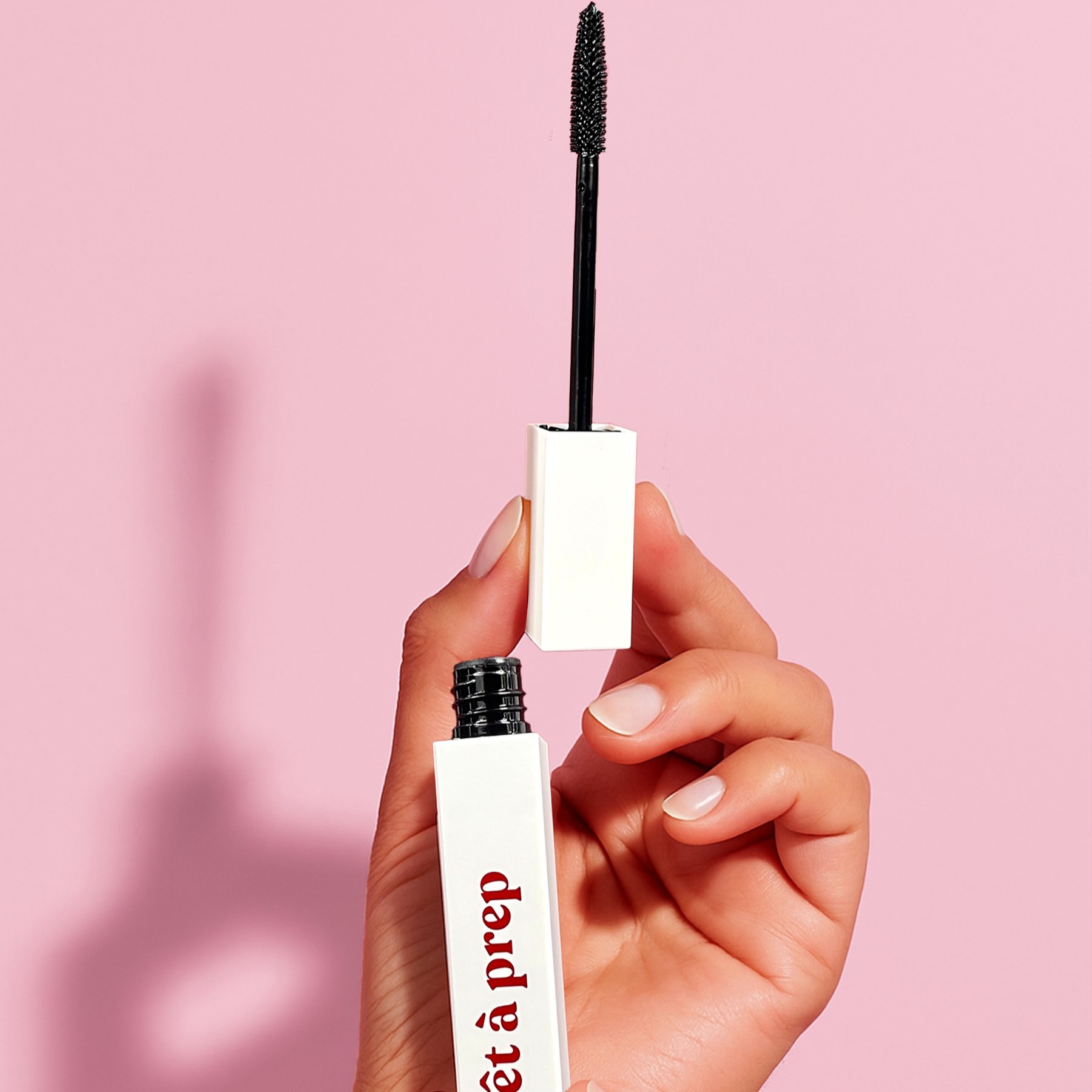 Mascara with 'pret a prep' branding held by a hand against a pink background